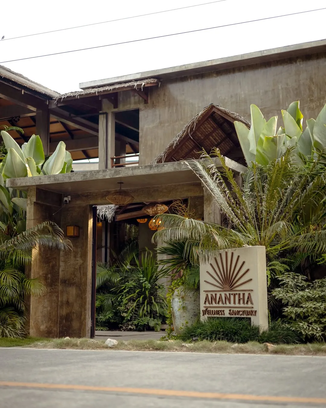The entrance gate and Anantha Wellness Sanctuary sign framed by tropical plants