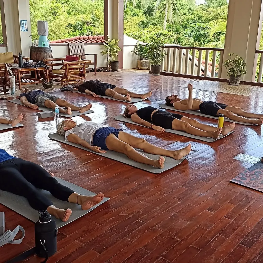 Students resting in savasana on the wooden floor at Anda Yoga Studio