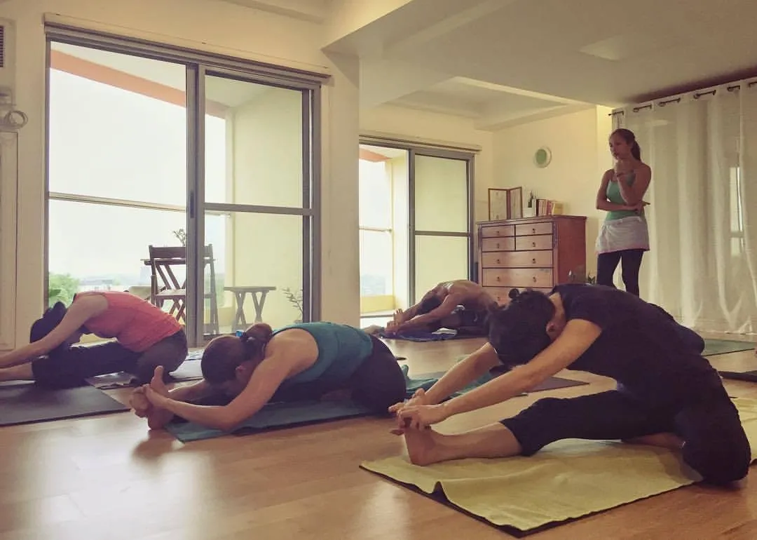 Students in seated forward folds by the windows during an Ashtanga Yoga Central class