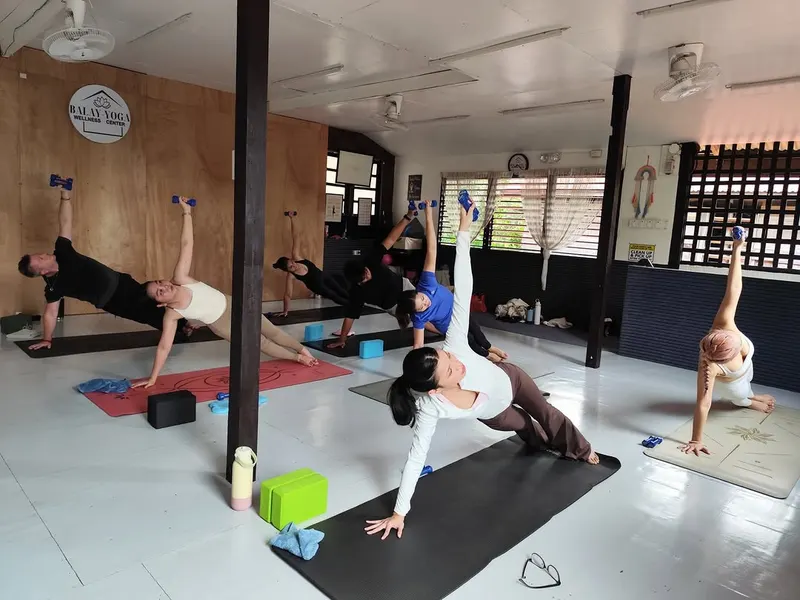 A yoga class in side plank across the white-floored practice room at Balay Yoga