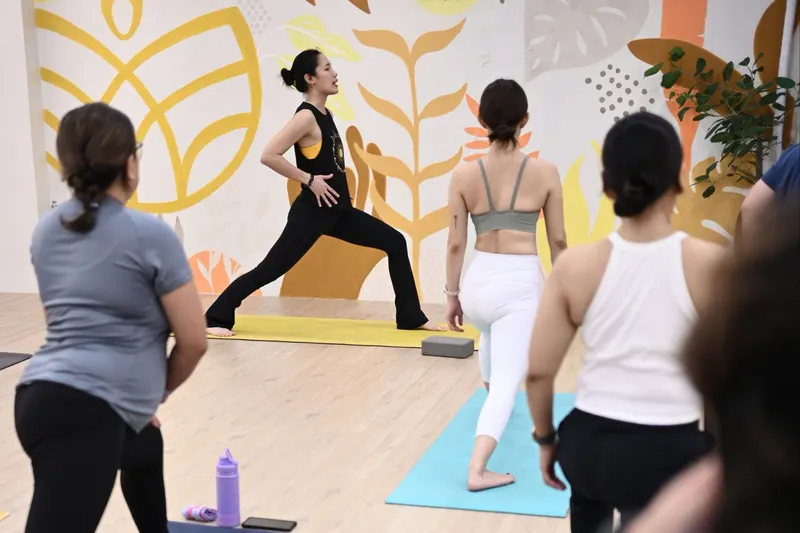 A teacher leading a warrior pose in front of the leaf-mural wall at BetterLife Studio