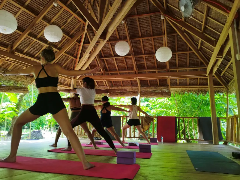 A yoga class in warrior pose in the open bamboo shala at Emerald House Village