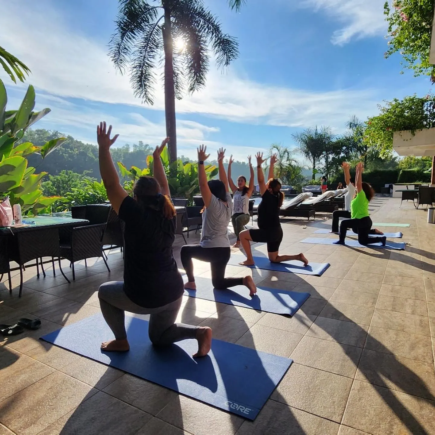 An outdoor Healing Iloilo class in crescent lunge on a palm-lined terrace