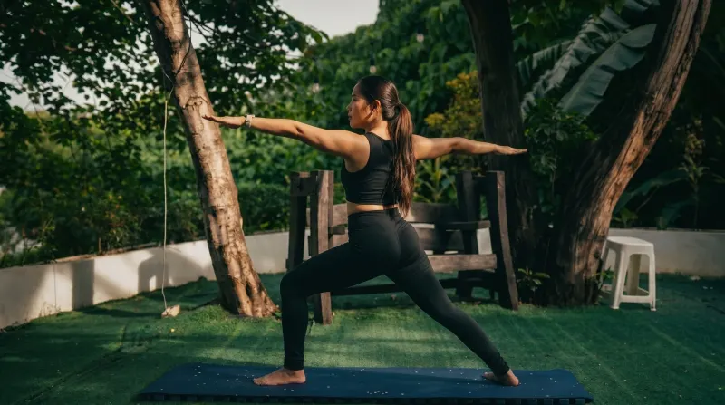 An Indian Yoga School PH teacher in warrior II on the garden practice lawn