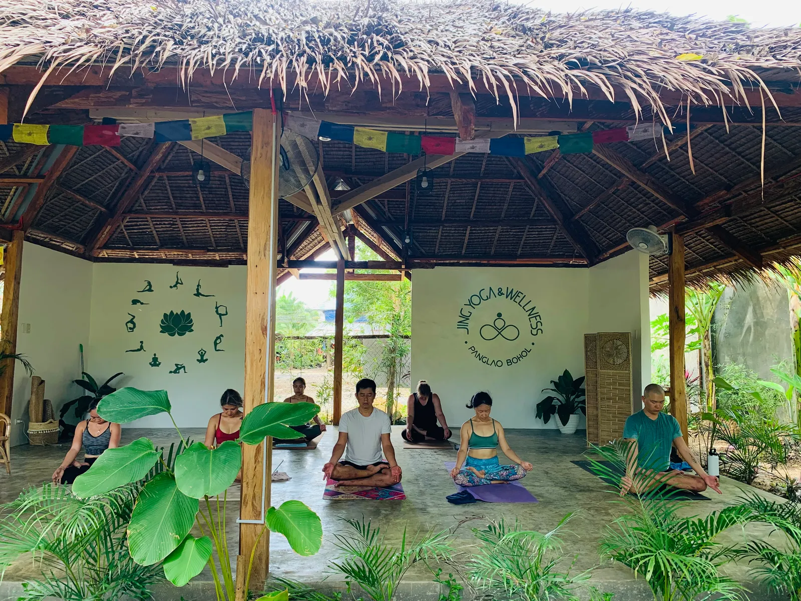 A class seated in meditation inside the open thatched shala at Jing Yoga and Wellness