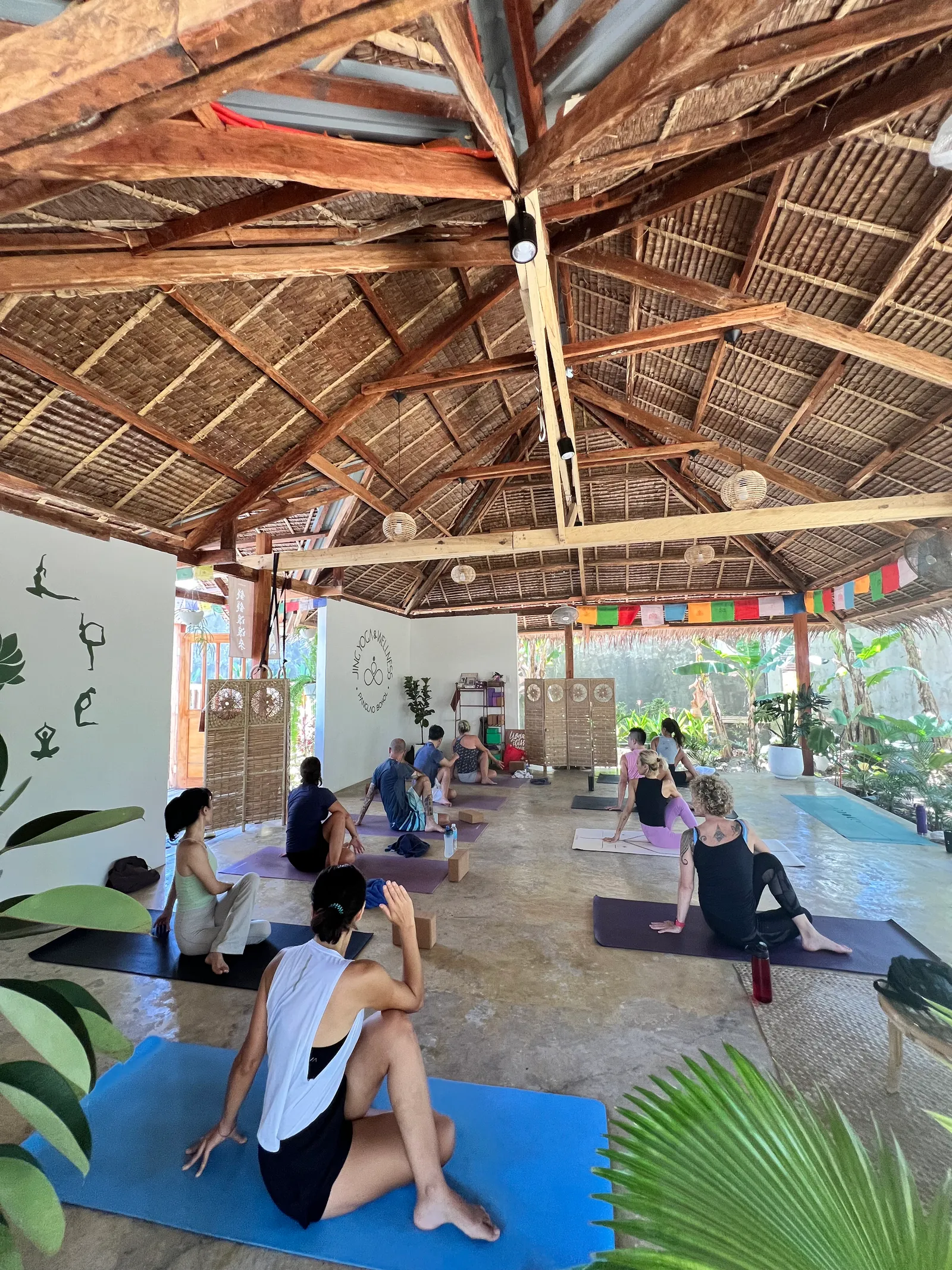 Students stretching on mats under the thatched roof at Jing Yoga and Wellness