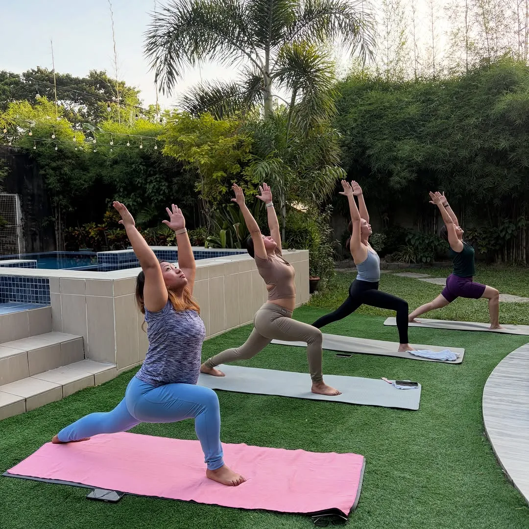 An outdoor Kaya Yoga class in crescent lunge on the lawn beside a pool