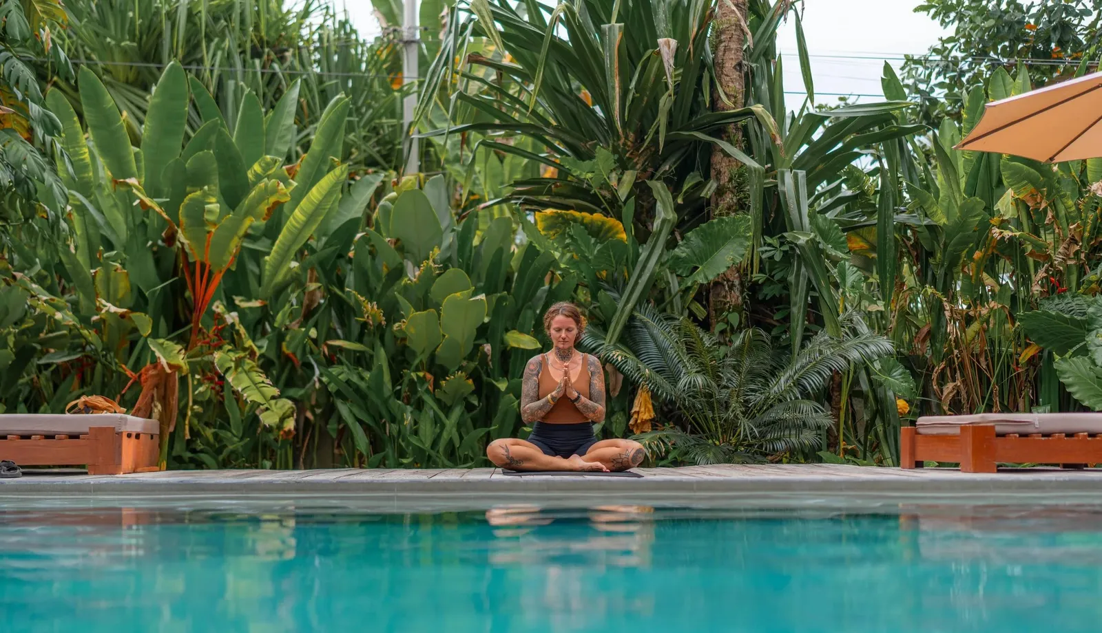 A person meditating at the edge of the pool among tropical plants at Kermit Siargao