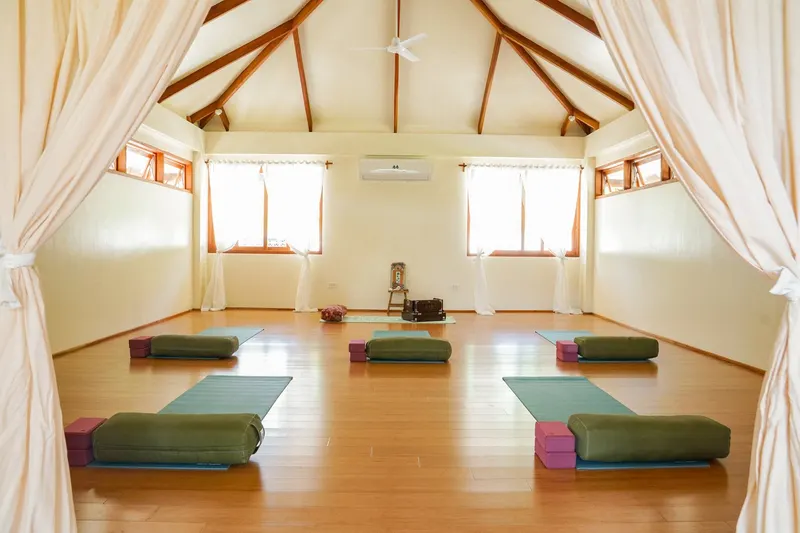 The bright practice room at Little Shell Yoga Shala with mats, bolsters and curtained windows