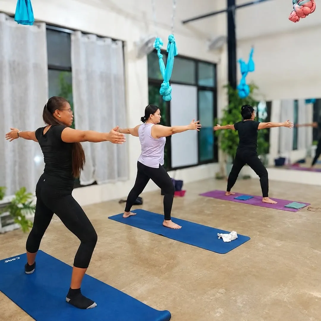 A Love Yoga World class in warrior II in a studio hung with aerial hammocks