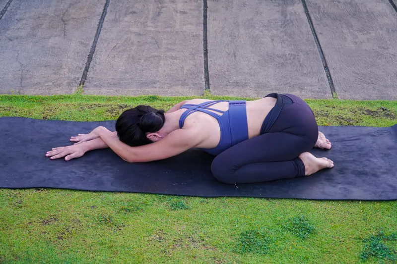 Practitioner resting in child's pose on a mat on a lawn