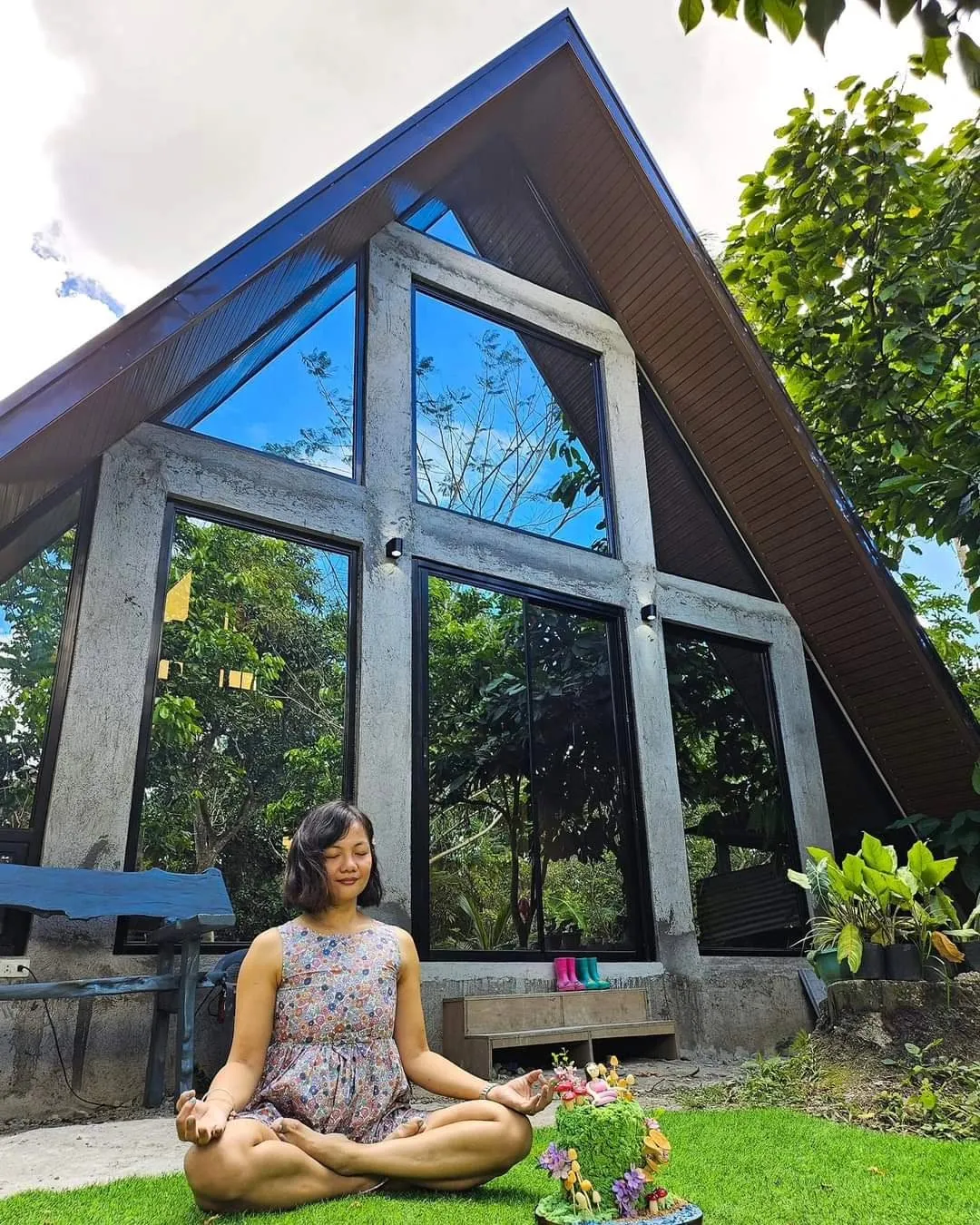 Glass A-frame studio building among trees with a teacher meditating on the lawn