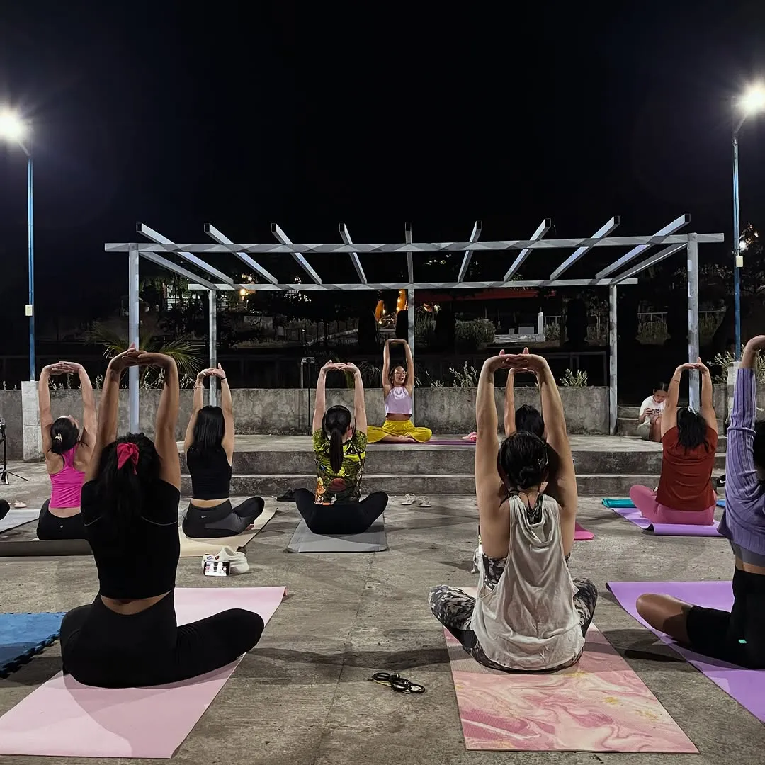 Evening outdoor yoga session on mats under a pergola, seen from behind
