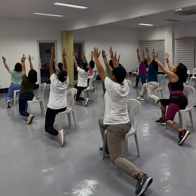 Group class in a low lunge with arms raised, seen from behind in a large hall