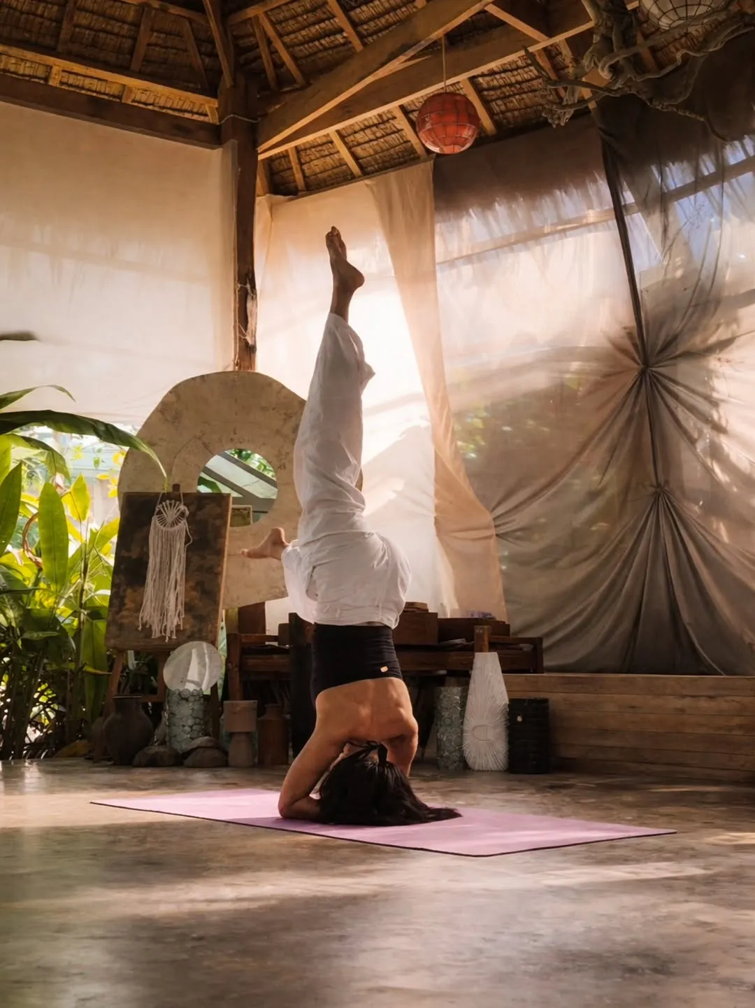 Practitioner in a headstand in a thatched shala with draped fabric