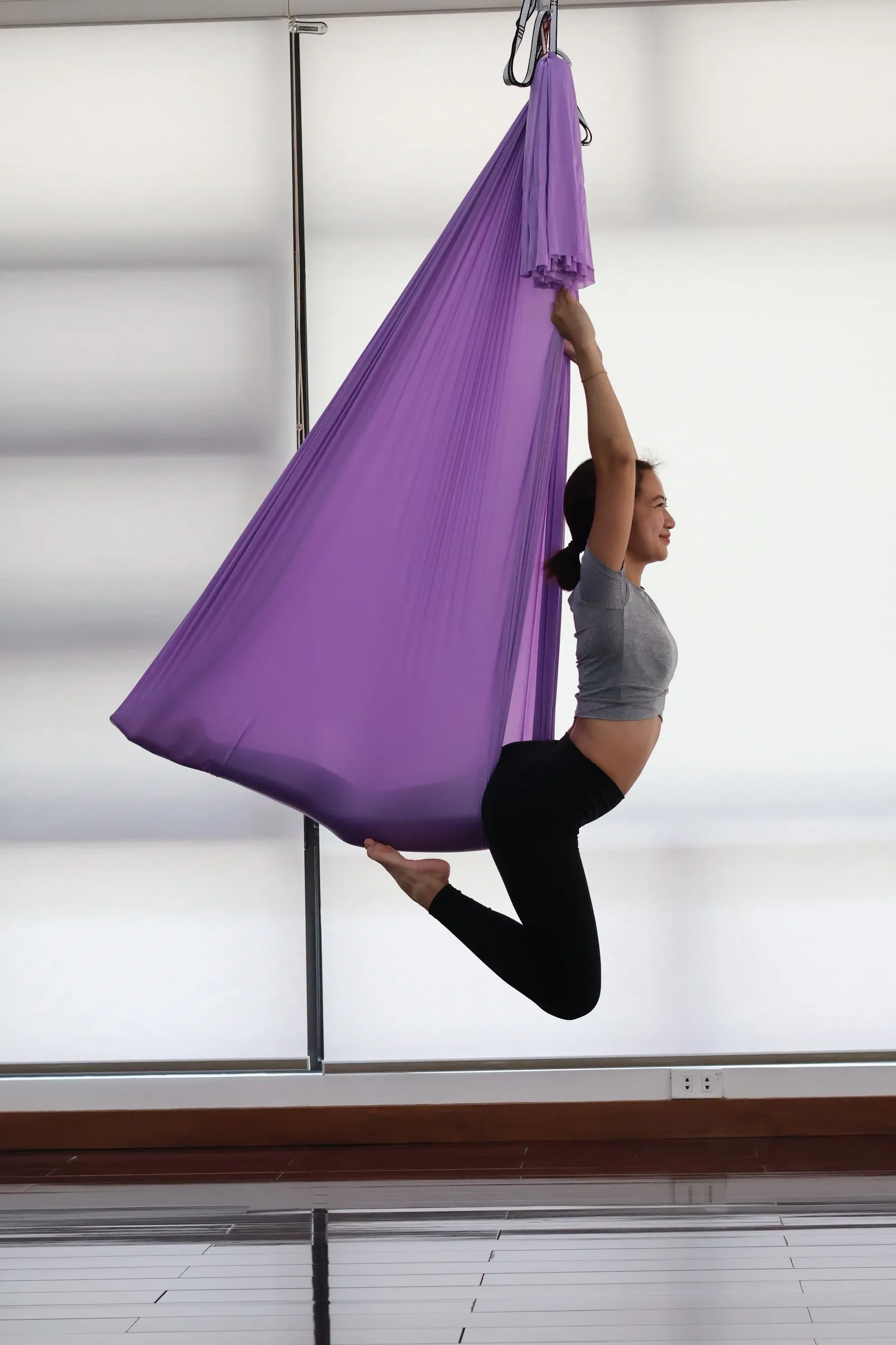Practitioner in a purple aerial hammock by a window