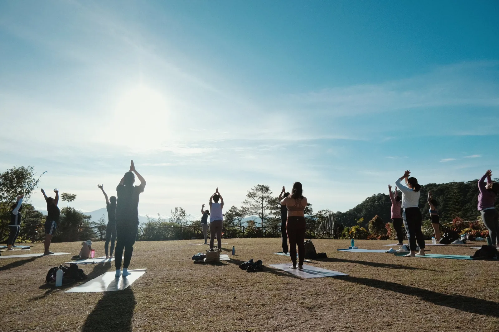 Outdoor group yoga session on a grassy hilltop under a bright sky