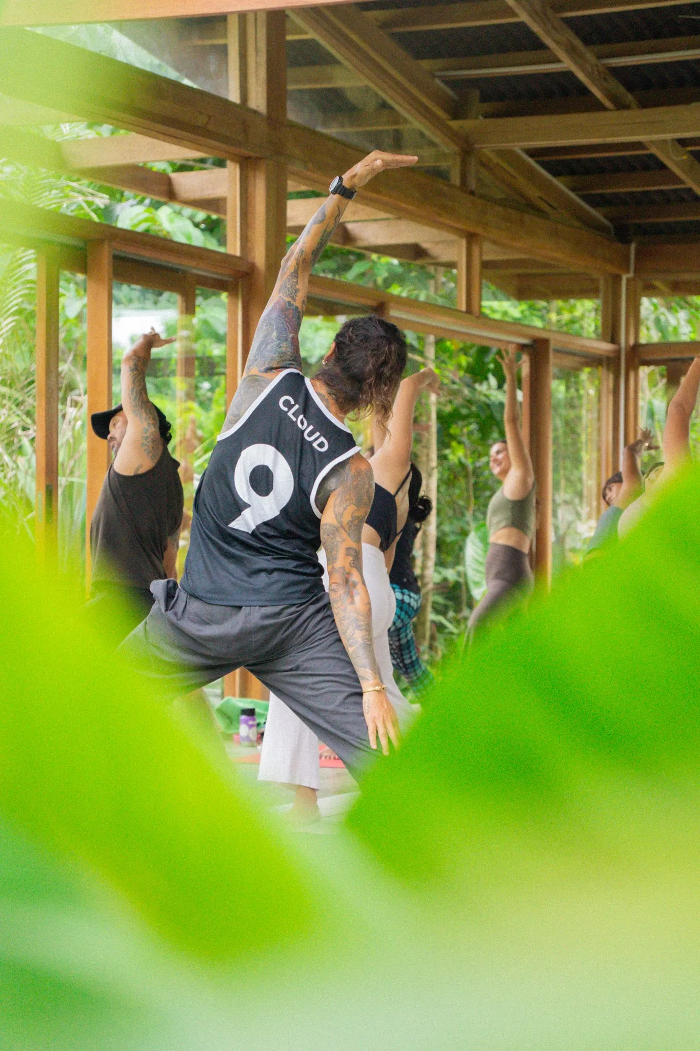 Students stretching in the shala, seen through leaves