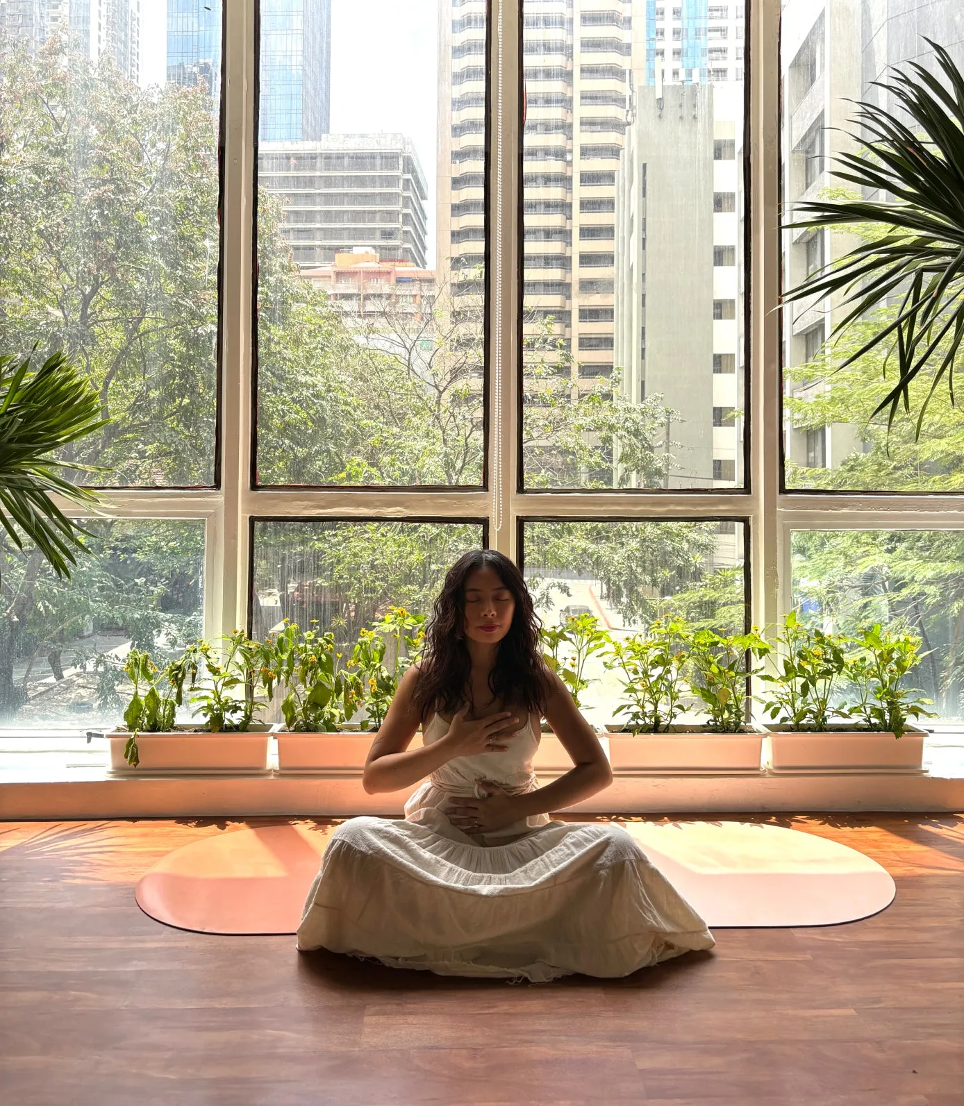 Teacher meditating on a mat in front of floor-to-ceiling windows with a city view