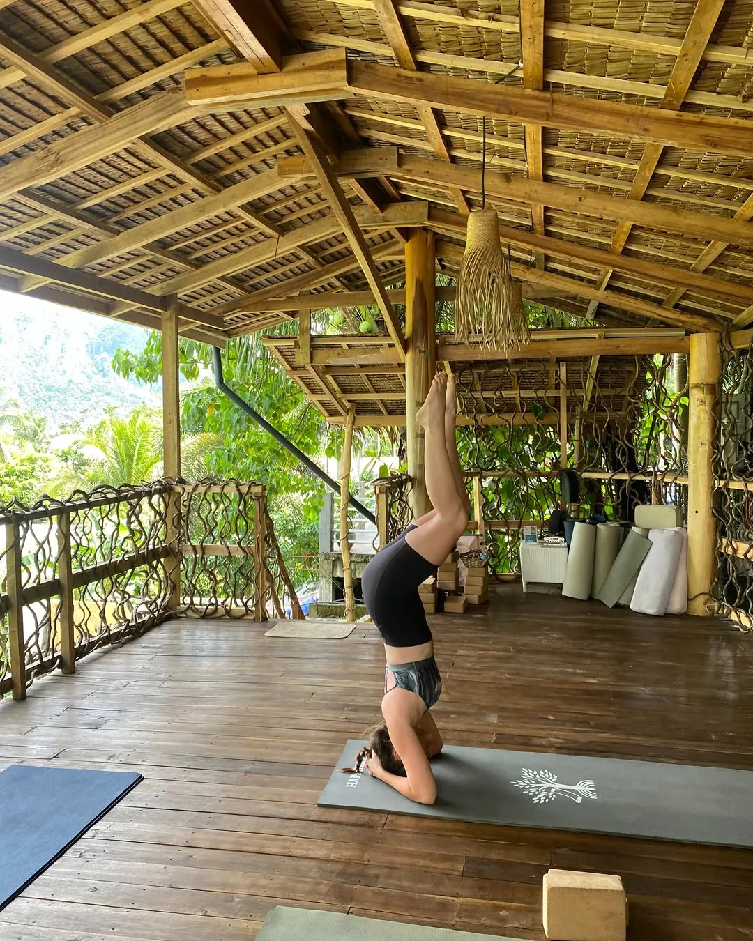 Practitioner in a headstand on a thatched yoga deck