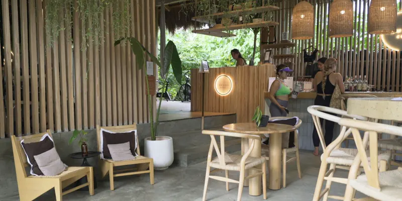 Open-air lounge with wooden chairs and tables under a thatched roof