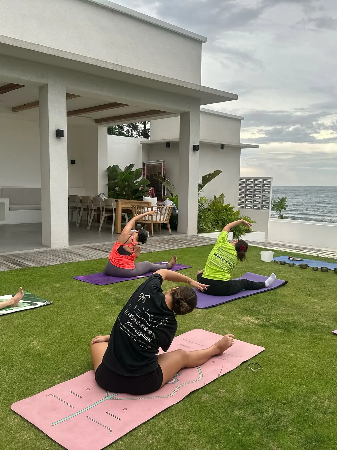 Students stretching on mats on a seaside lawn beside a white building