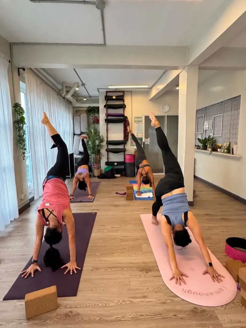 Students in a three-legged dog pose with a wall rope rack behind
