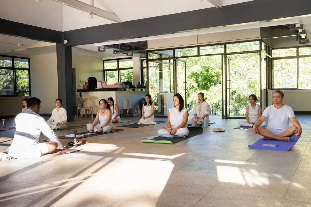 Seated class on mats in a sunlit open-sided hall