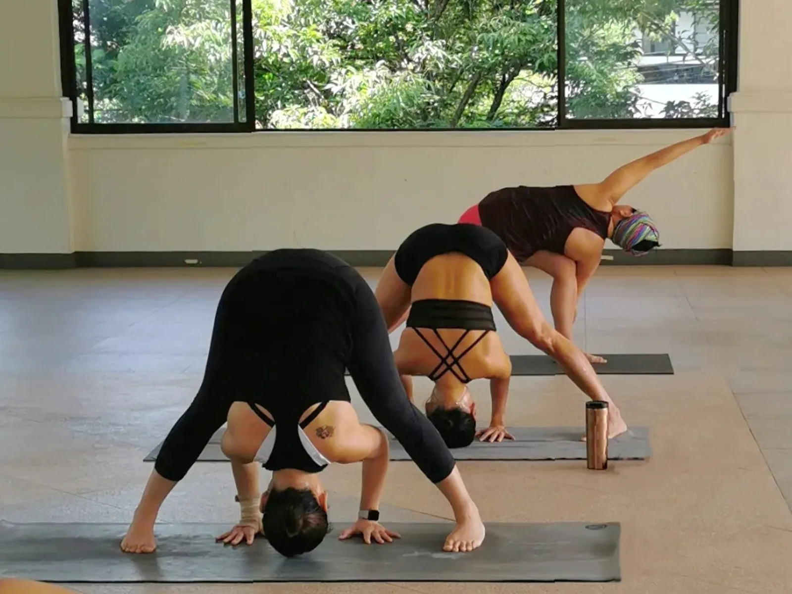 Practitioners in wide-legged forward folds in a studio with large windows