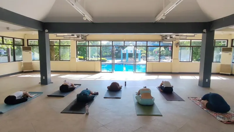 Students resting on mats in a large open hall with a view of a pool