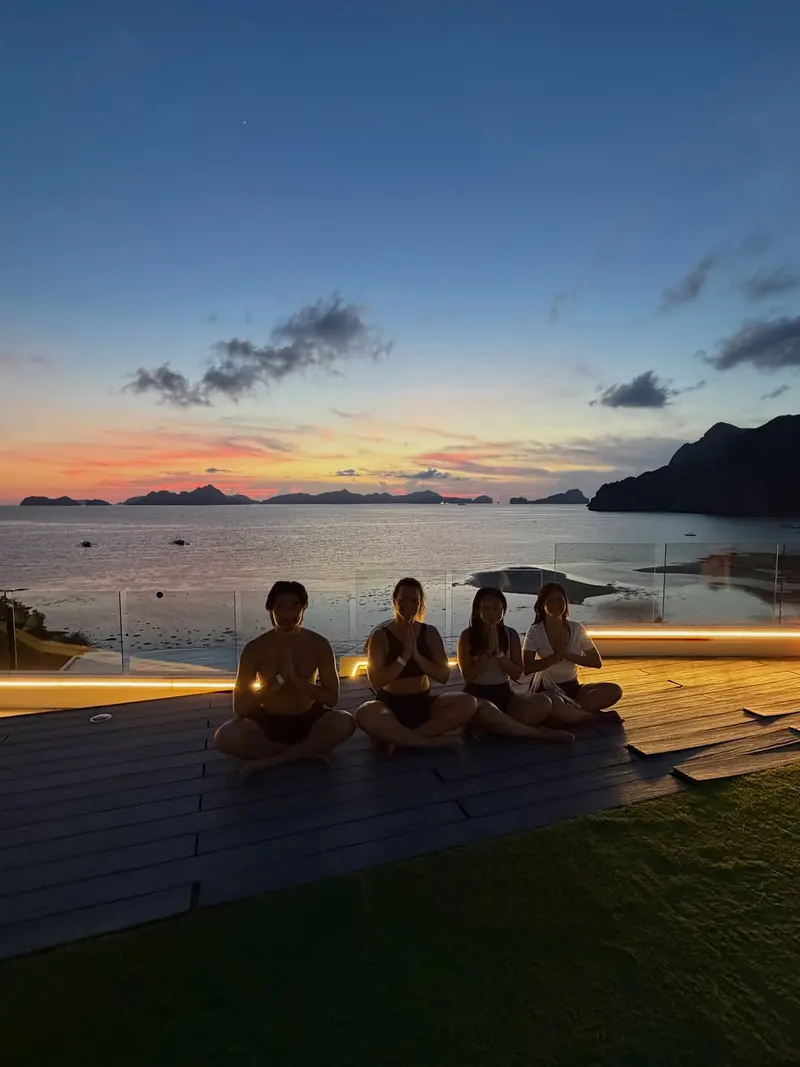 Small group meditating on a deck at dusk overlooking the bay and islands